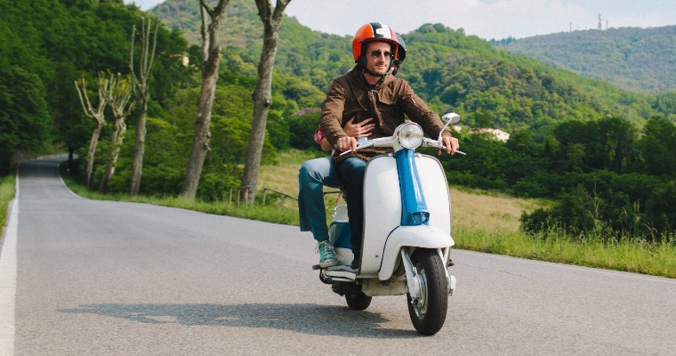 Two people riding a moped on an empty street, both wearing helmets