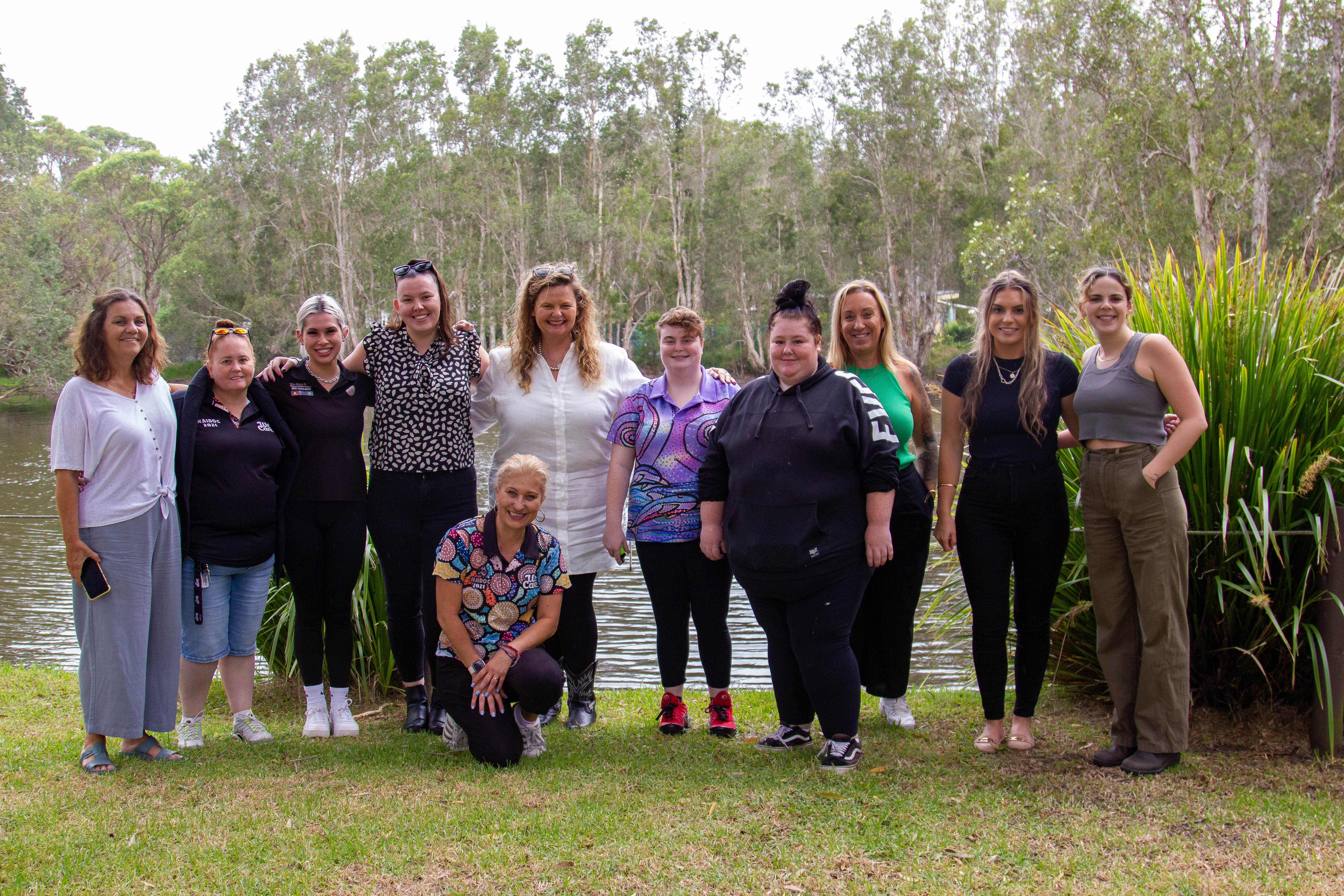 Eleven female participants of We Care's Sista Circle program standing outdoors by the river smiling