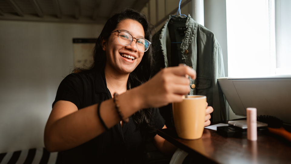 Person smiling, stirring a hot drink in a mug.