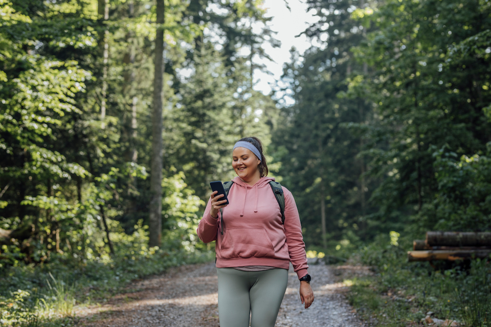 A person walking through the forest on a hike looking at their smartphone.