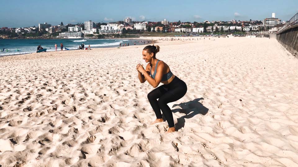 A person doing squats on a beach.