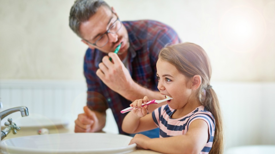 A father and daughter brush their teeth together.