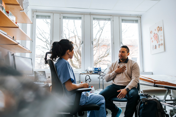 A male patient explains his symptoms to a doctor in a consultation room