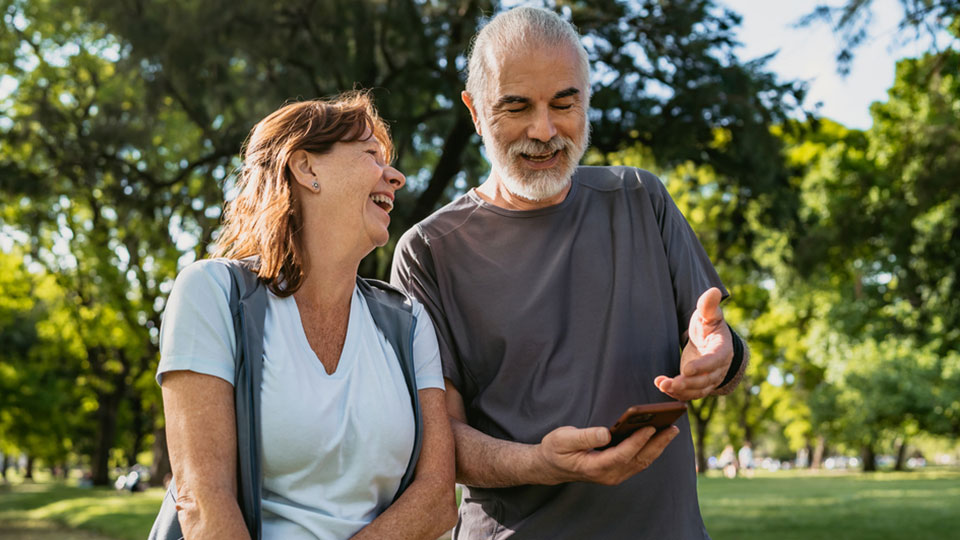 A middle-aged couple laugh as the man looks at his phone.