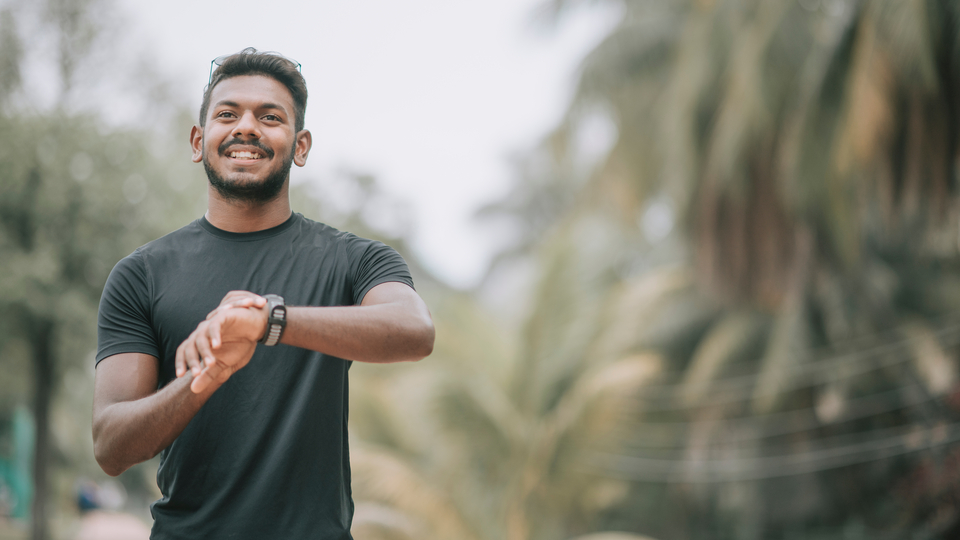 A man in a gray shirt checking his fitness watch outside in a park.