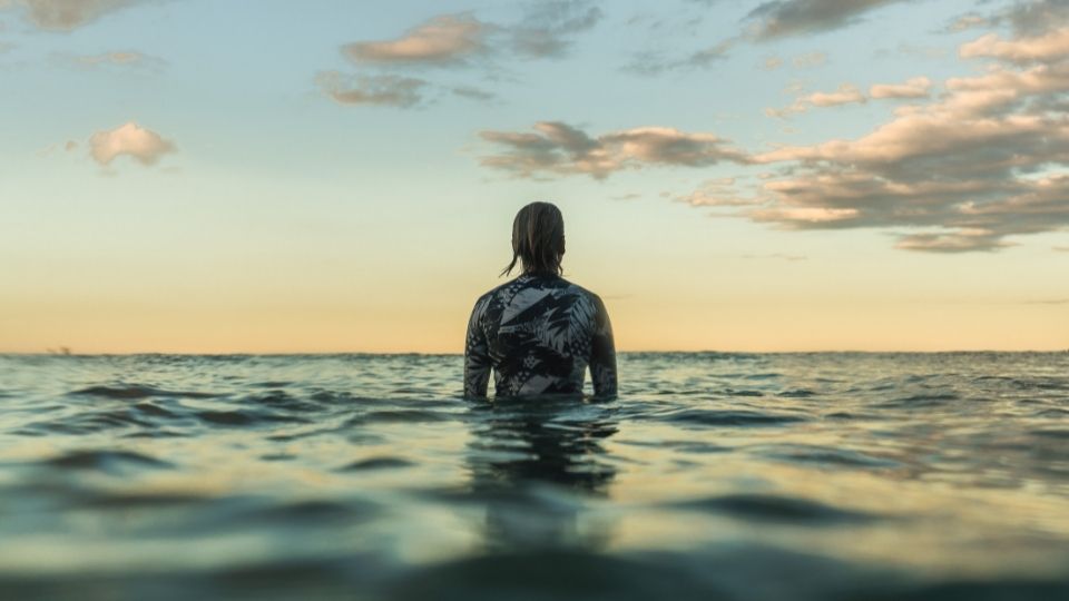 Layne Beachley sitting on a surfboard in the ocean looking into the distance.