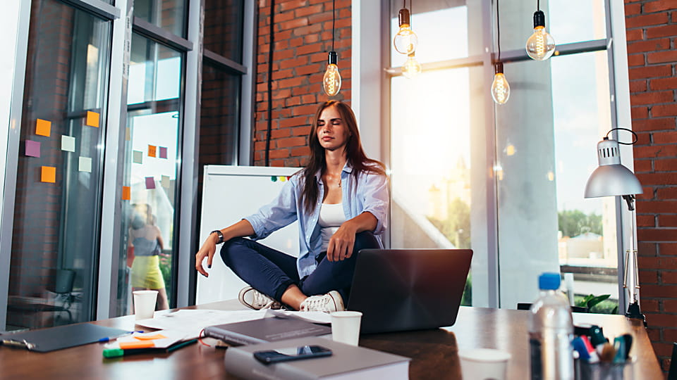 Person sitting on top of their desk at work, meditating.