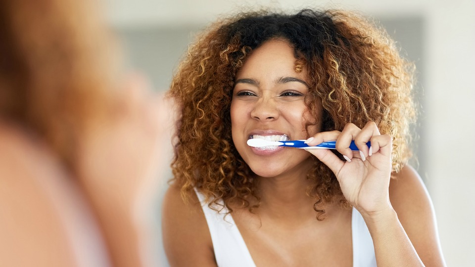 Woman brushing teeth in mirror.