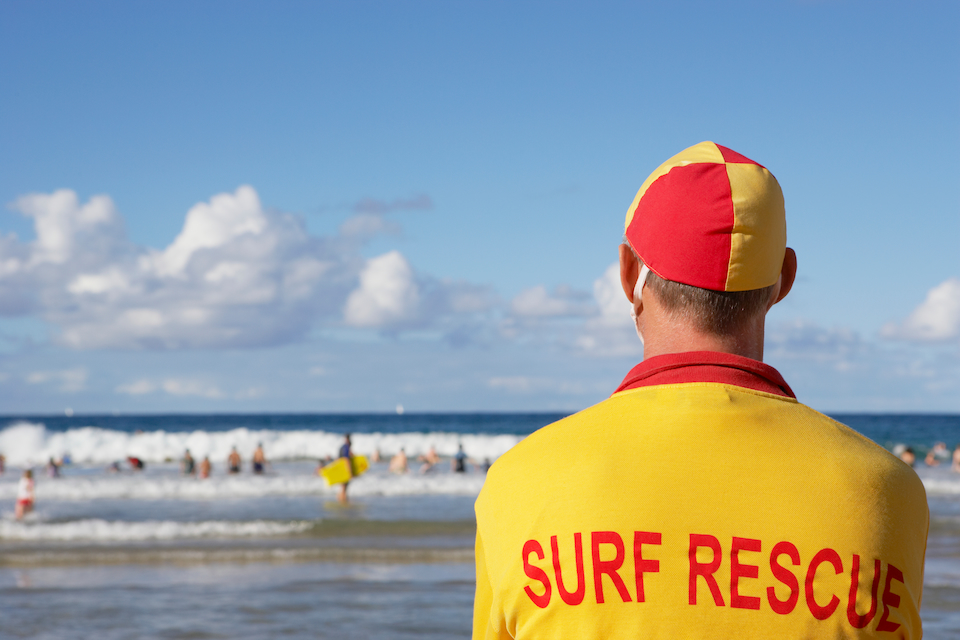 Australian lifeguard monitoring the beach, angle shows back of lifeguard looking out toward the ocean.