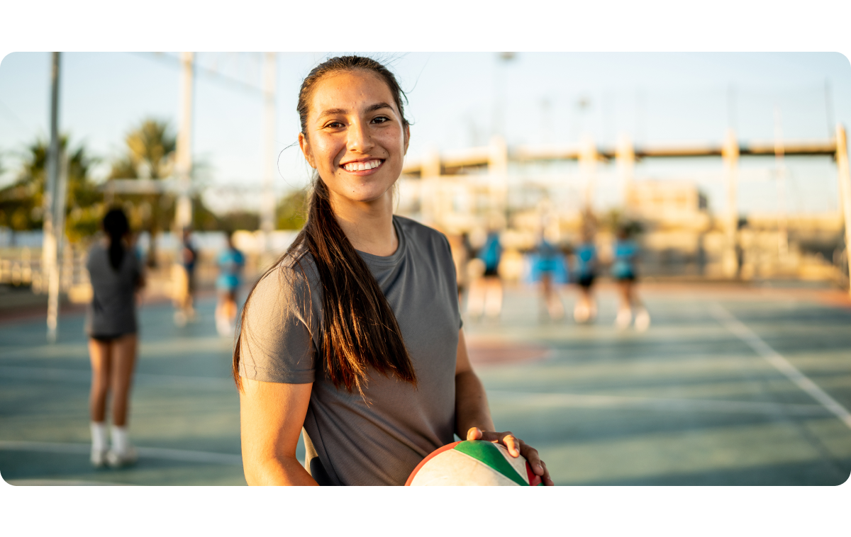 A young woman playing netball is standing on the court, smiling at the camera.