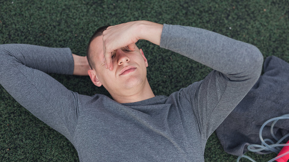 A man lays on the ground and rubs his eyes.