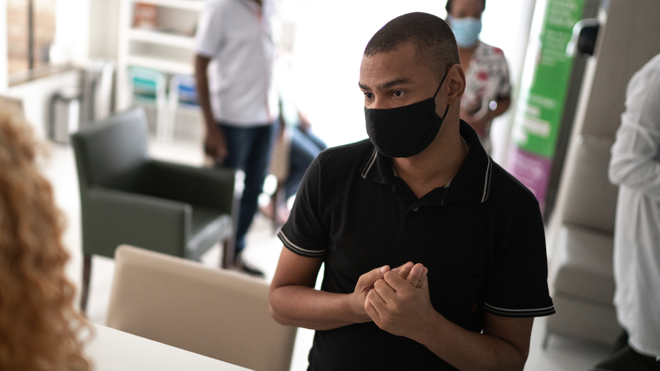 A young man wearing a black face mask talks to a customer.