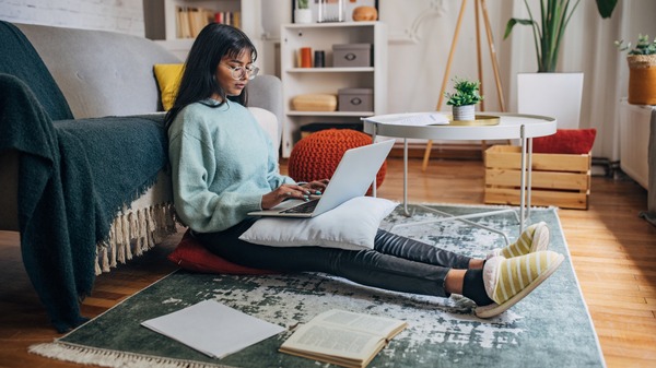 Person sitting on the floor using their laptop, with documents and books across the ground.