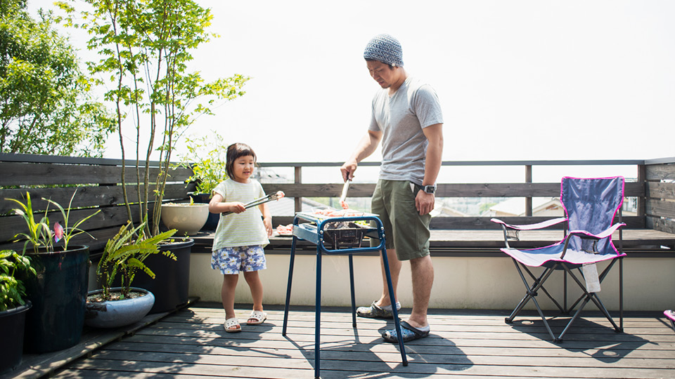 Man cooking barbeque with daughter on balcony.