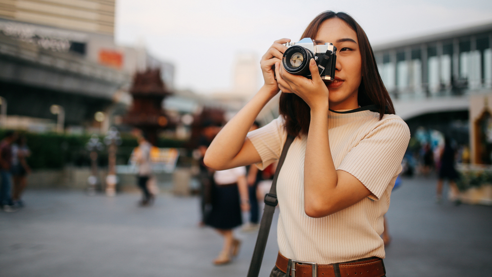 Young dark haired woman holding a vintage camera while travelling overseas.