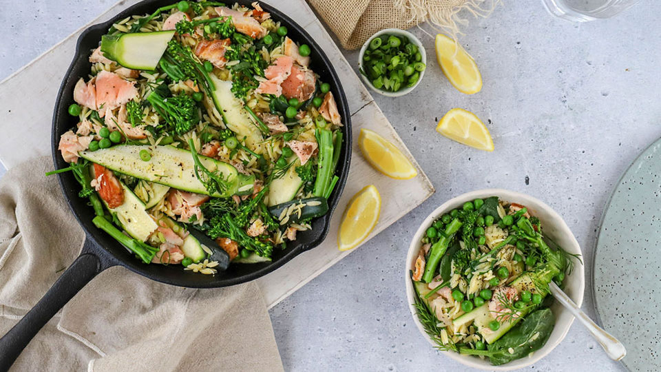 Salmon, zucchini and risoni in a cast iron pan with a bowl of the meal on the side.