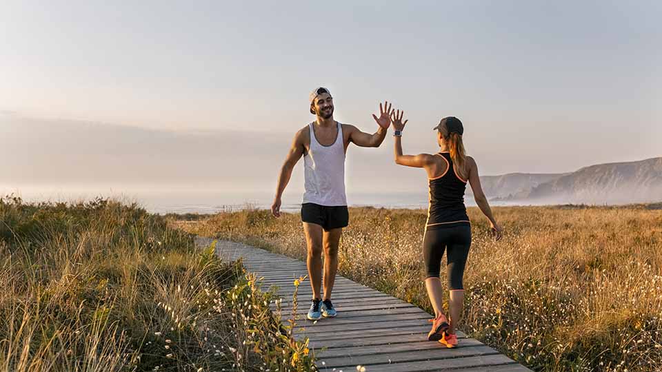 A man and woman in activewear walk past each other while giving a high five