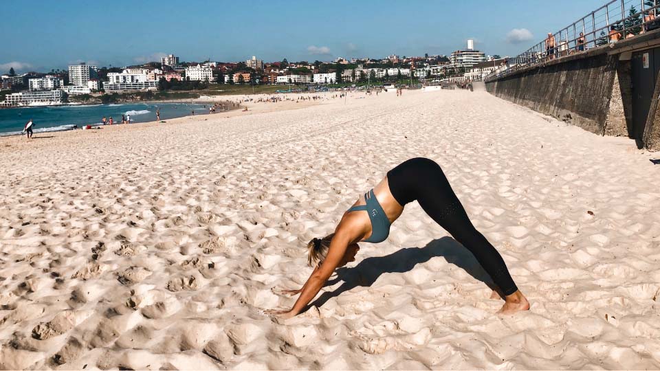 Cassey Maynard doing a downward dog yoga pose at the beach.