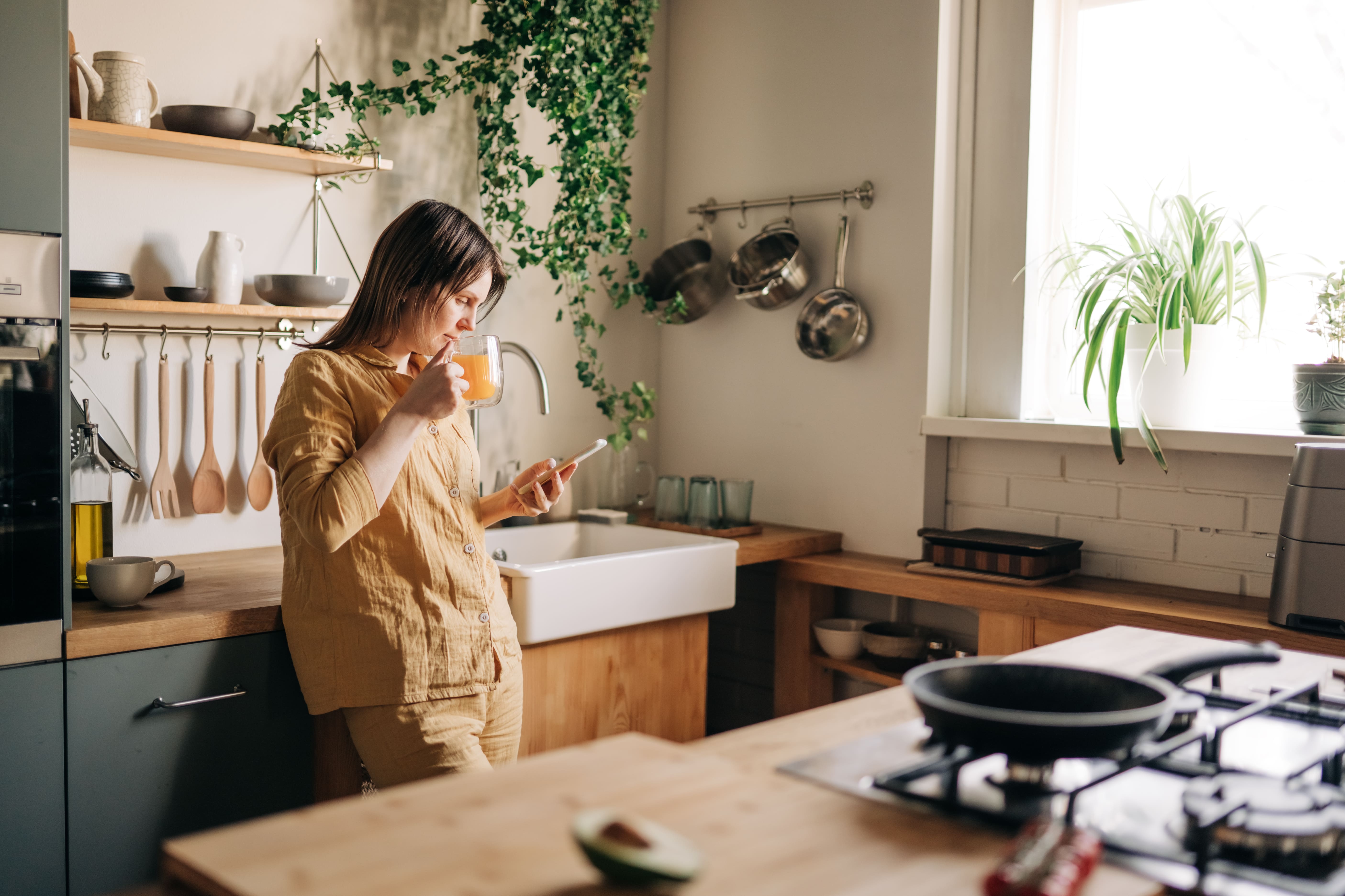 woman in her kitchen drinking tea, reading news on her phone