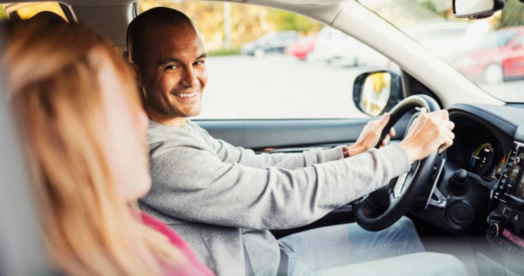 A man driving in a car smiling to a woman in the passenger seat