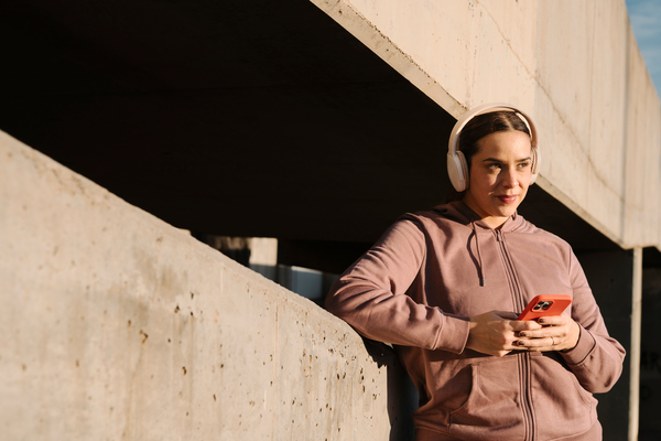 Woman with headphones leaning against concrete wall looking at phone
