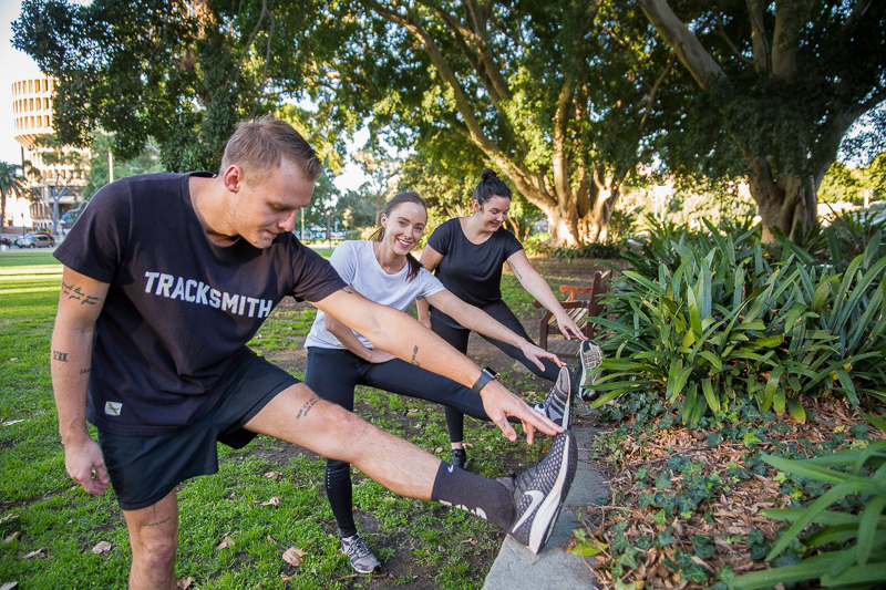 A man and two women stretching their left leg at the park