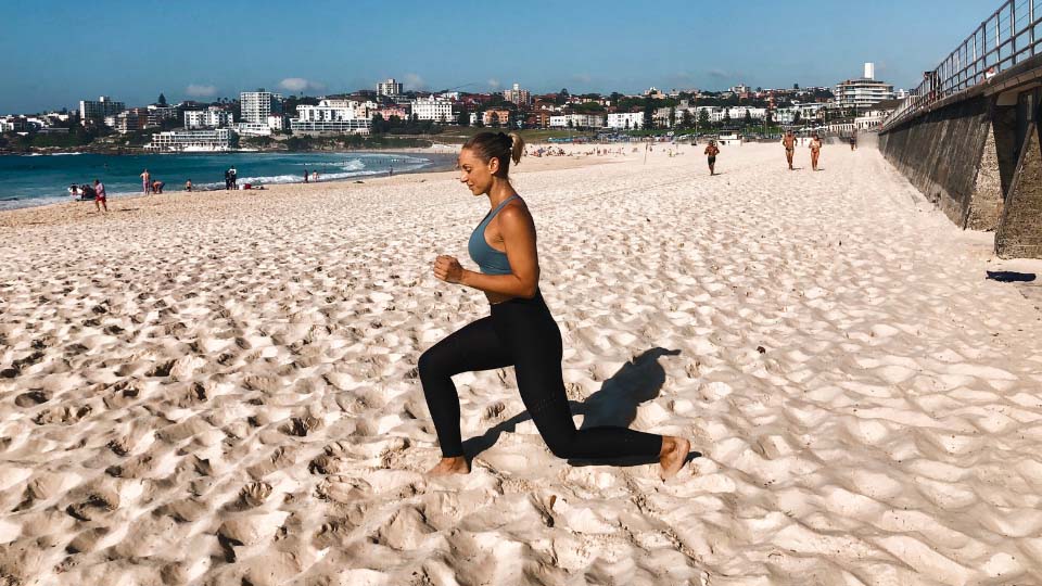 A person doing jump lunges on a beach.