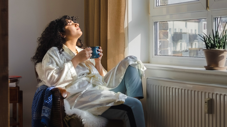 Woman enjoying sunlight sitting on chair near window at home.