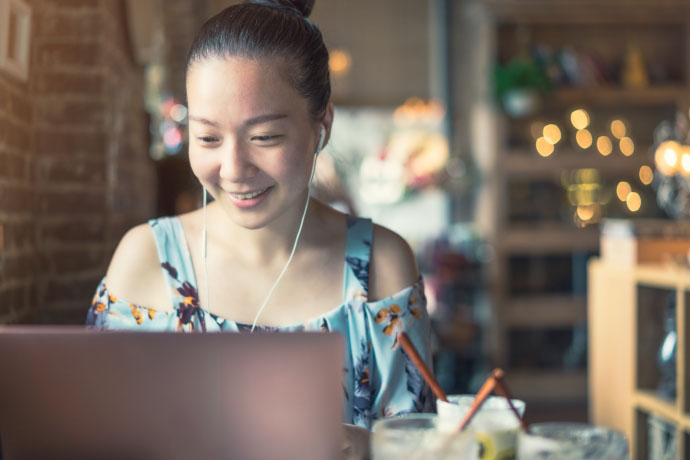 A woman smiles at her laptop screen with headphones plugged in.