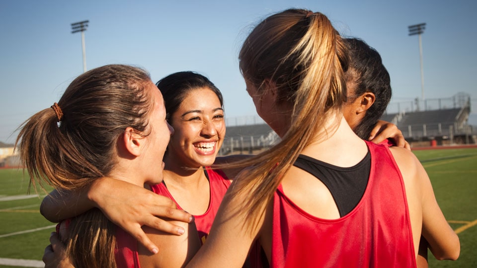 A team of four young women huddling together on a sports field.