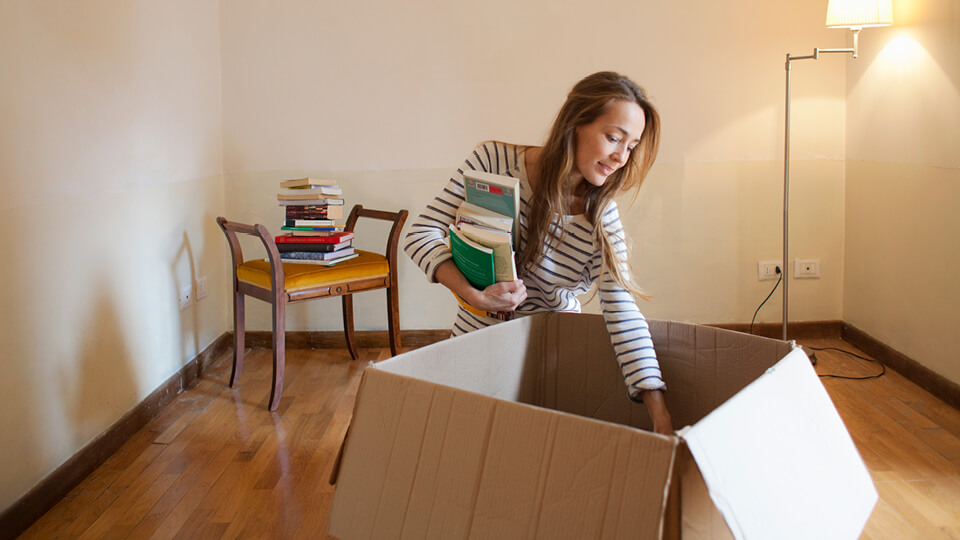 A young woman unpacks a stack of books from a cardboard box