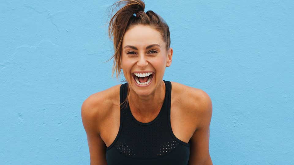 Close up of a woman standing in front of a blue wall candidly laughing.