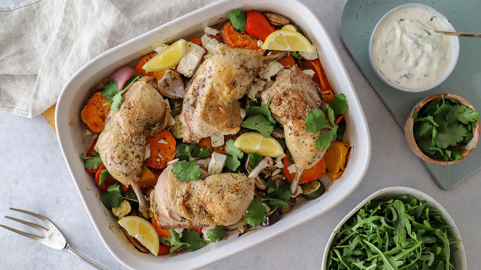 Chicken in tray with vegetables, herds and dressing on the side.