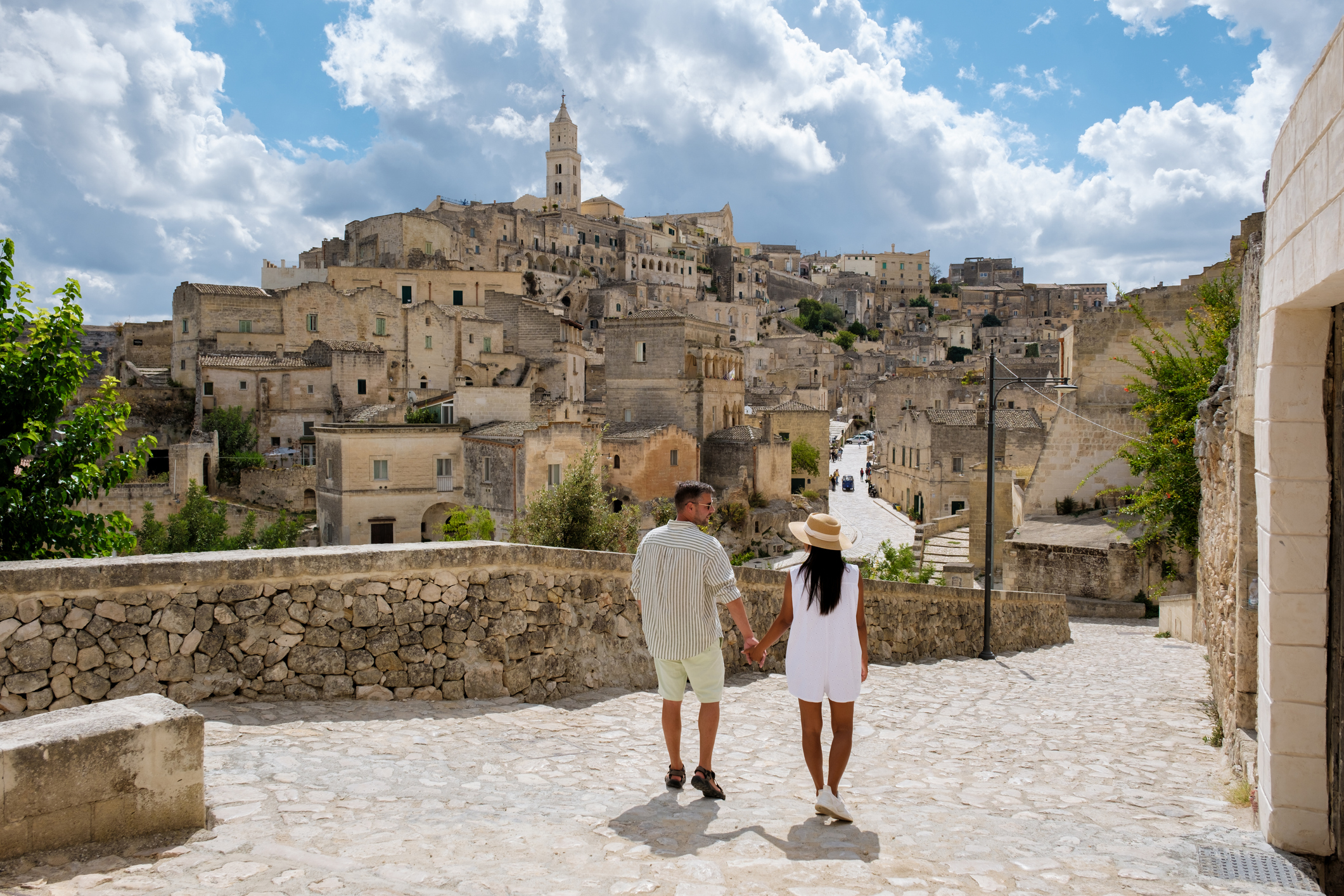A couple strolls hand in hand along a cobblestone path, surrounded by the ancient cave dwellings of Matera, Puglia