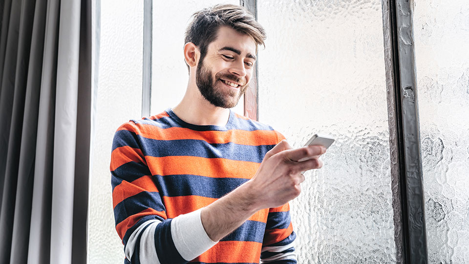 A man smiling as he looks at his phone.