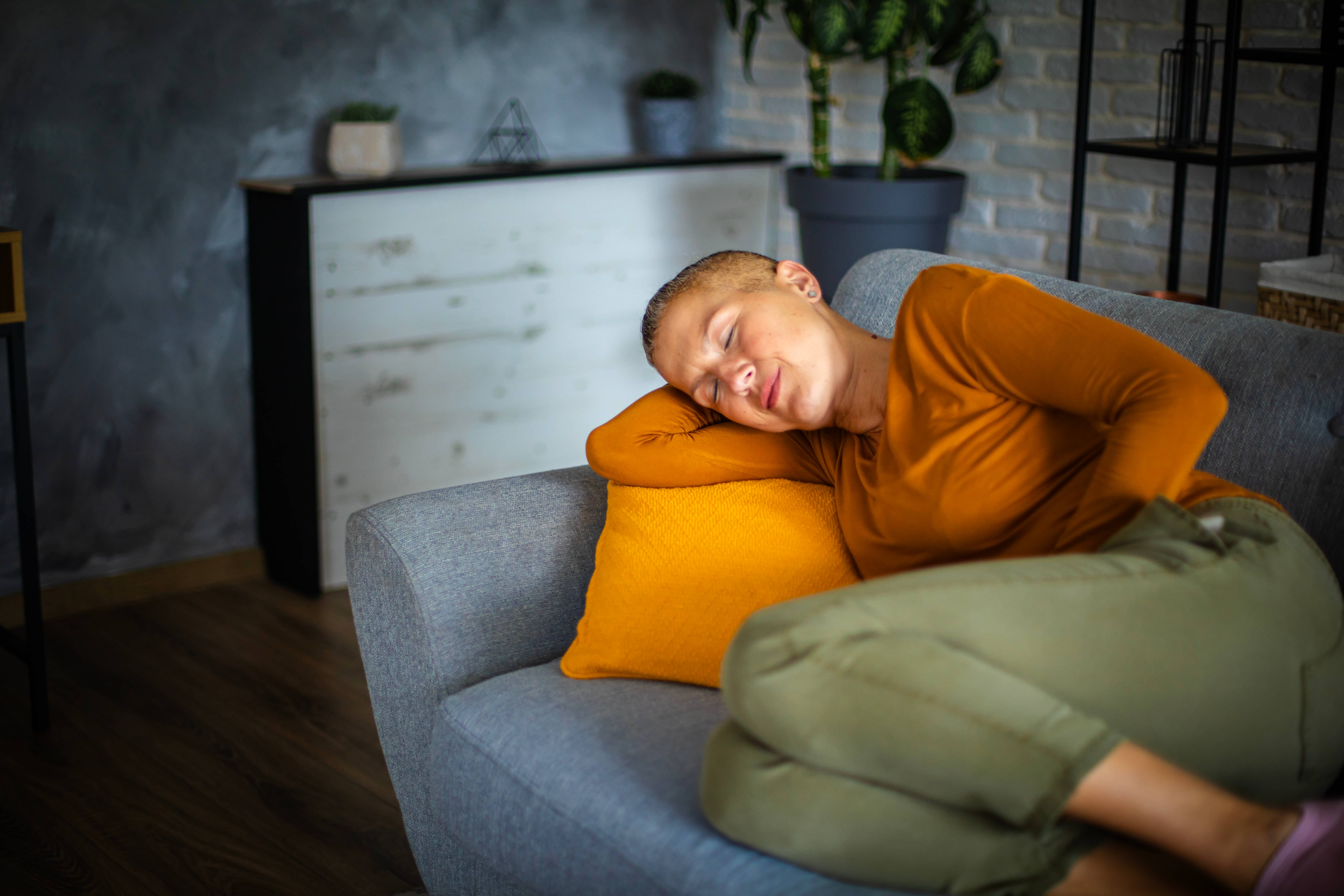 Person laying on a lounge, clutching at their abdomen.