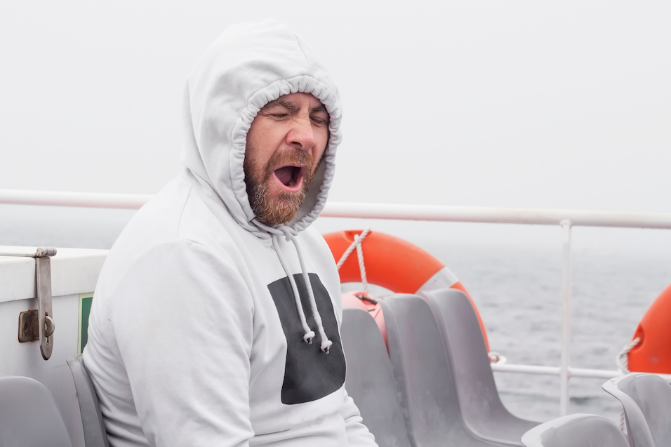 Man wearing a hoodie experiencing motion sickness on a ferry.