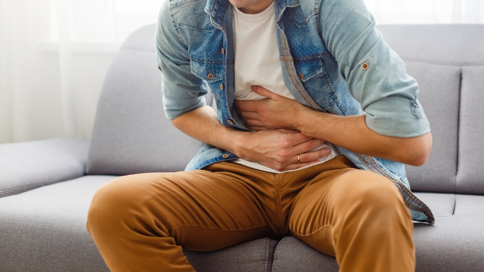 A young man hunching over on the couch, holding his abdomen.