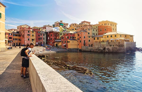 A man leaning over to look at the ocean, in front of one of the famous Cinque Terre towns