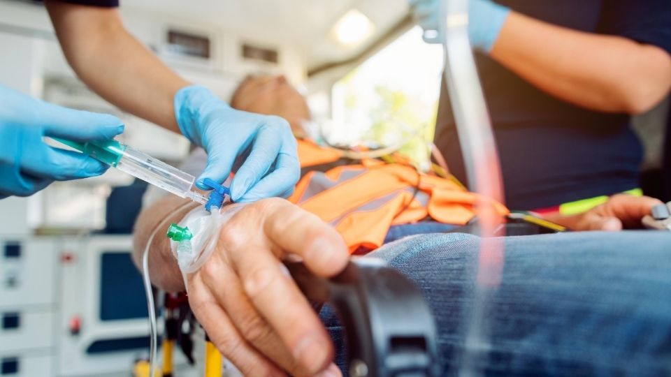 Person lying on a stretcher in an ambulance having medication injected into a tube.