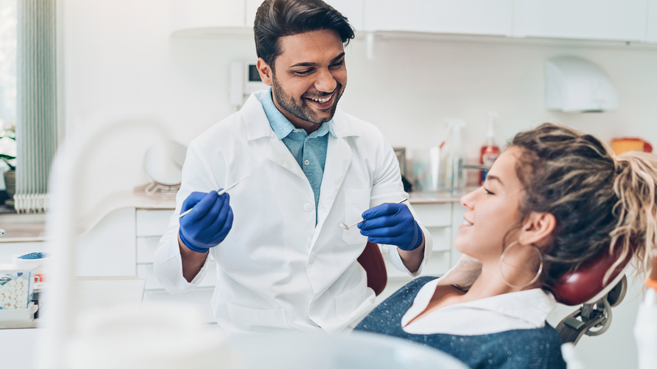 A person sitting in the dental chair while a young dentist explains the procedure.