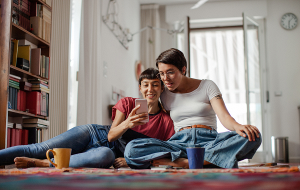 Two women sitting on the floor look at a smartphone