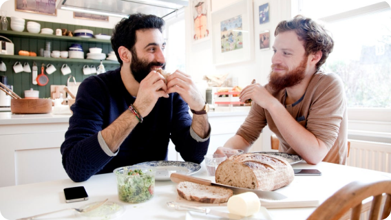 Two people sitting at kitchen table eating slices of bread.