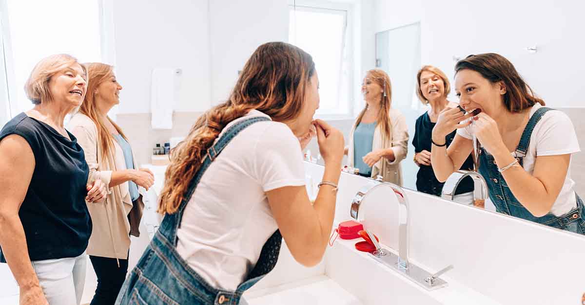 A group of women in the bathroom chatting as one flosses.