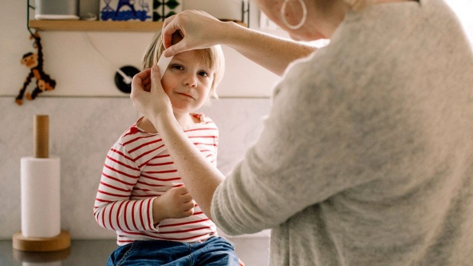 Adult applying a band aid to a child's head.