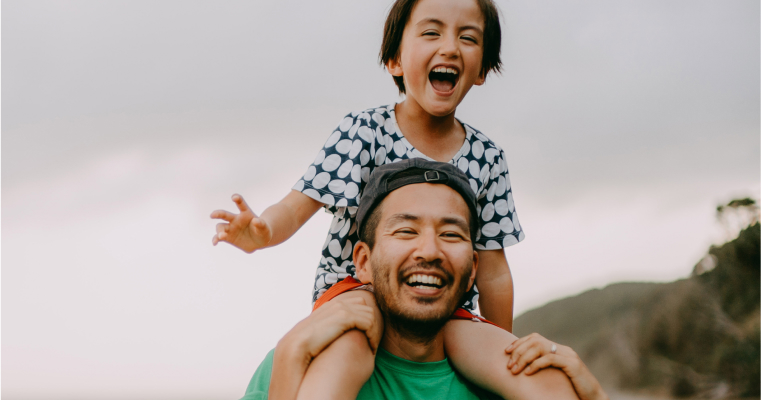 A boy sitting on his fathers shoulders, both smiling and laughing