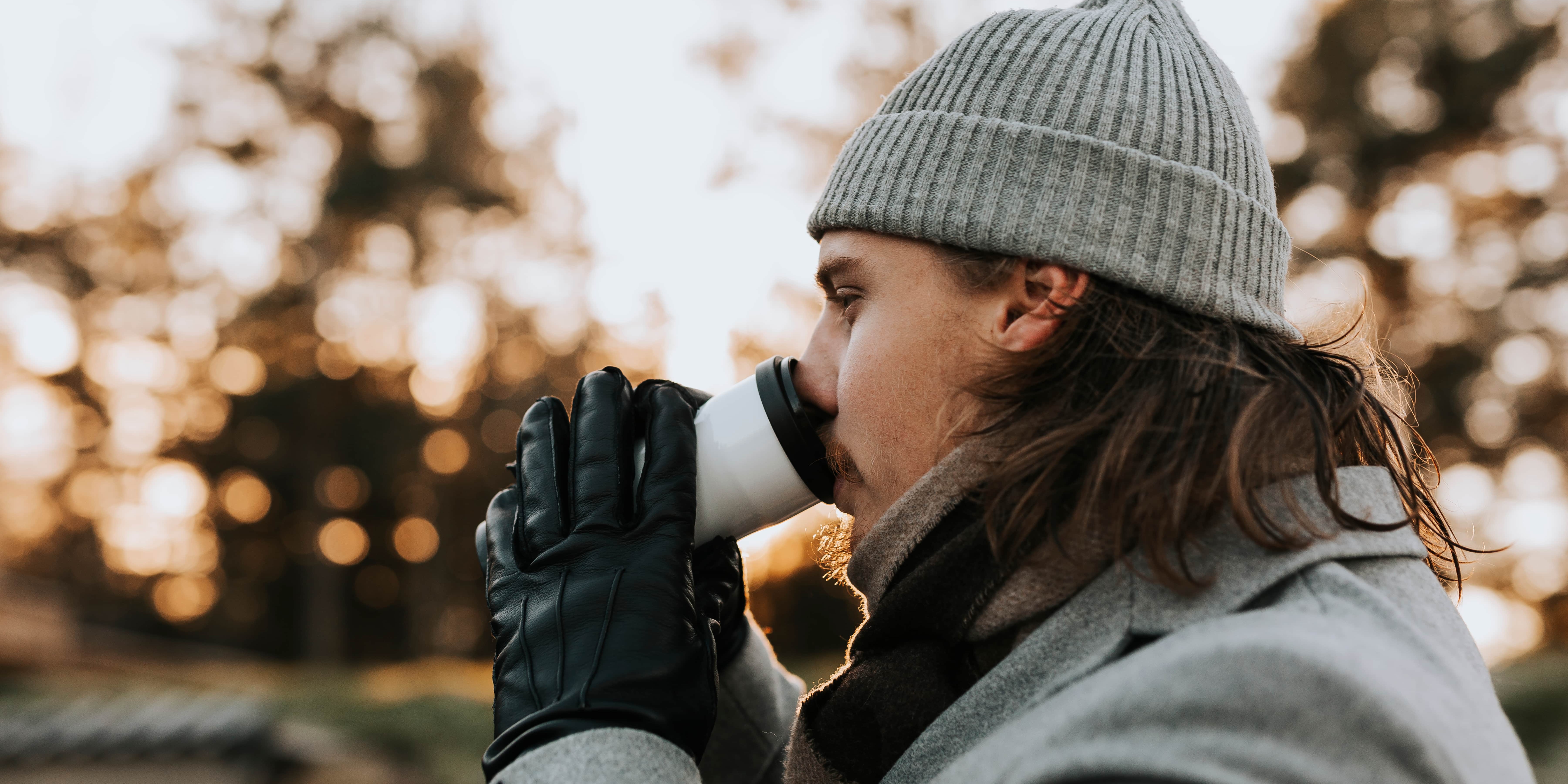 A man wearing a beanie drinks a warm cup of coffee.