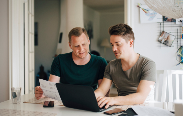 Two men sit at a desk looking at a laptop