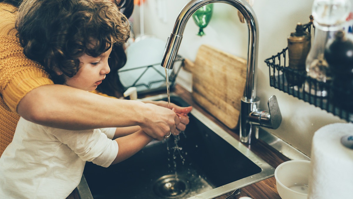 A child washing their hands with the guidance of an adult.