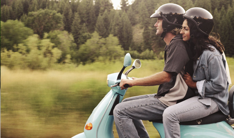 A man and a woman on a moped, both wearing helmets